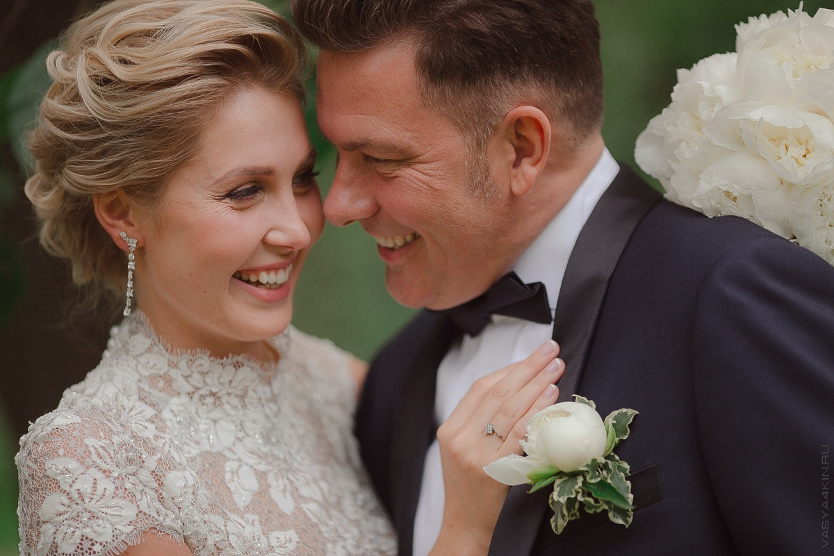 Невеста и жених смотрят друг на друга сквозь прогулочное зеркало на фоне маленькой деревушки, создавая атмосферу покоя и слияния с природой