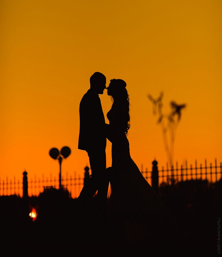 Молодая пара, стоящая на фоне украшенного фонтана с нежным сочетанием цветов и искусственного освещения