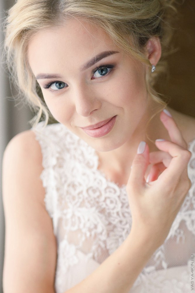 Невеста и жених стоят на дороге перед входом в свадебный зал, обнявшись и улыбаясь друг другу