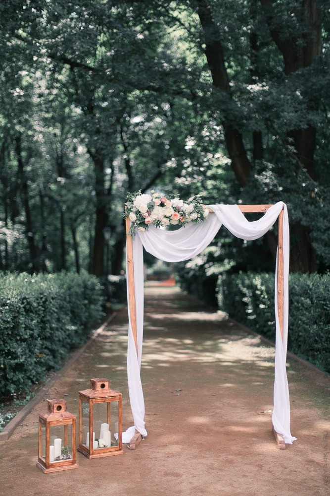 Молодожены прогуливаются по дорожке, усыпанной белыми и красными лепестками, на фоне дворца в Ярославле