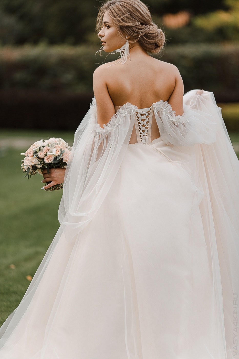 Молодой, наблюдающий за невестой, идущей по декорированному оградой уличному переходу, с улыбкой на лице