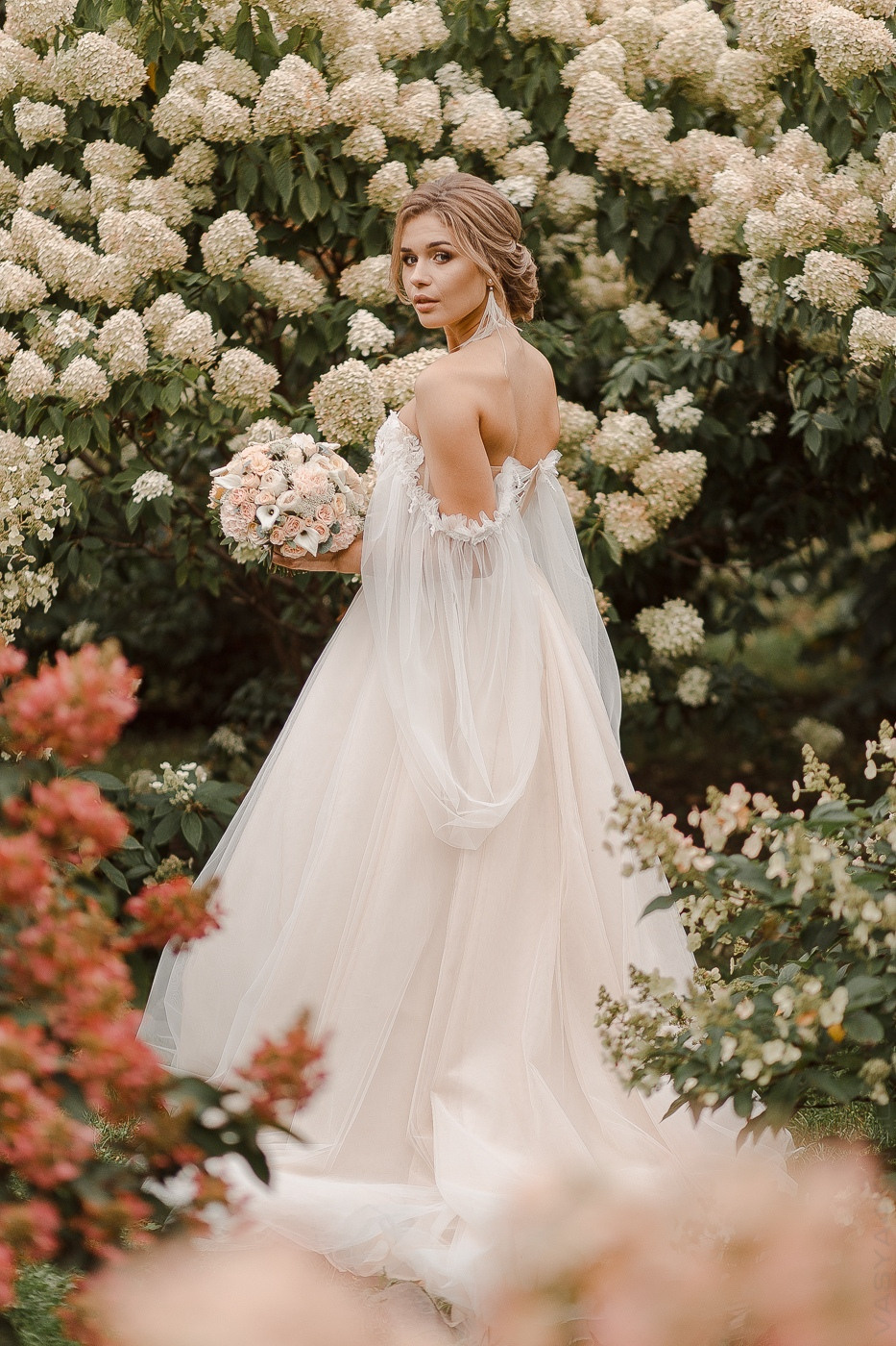 Фотография с дорогой свадьбы в Ярославле, где молодожены идут по дорожке с живыми цветами и светящимися факелами, вокруг них летают бабочки