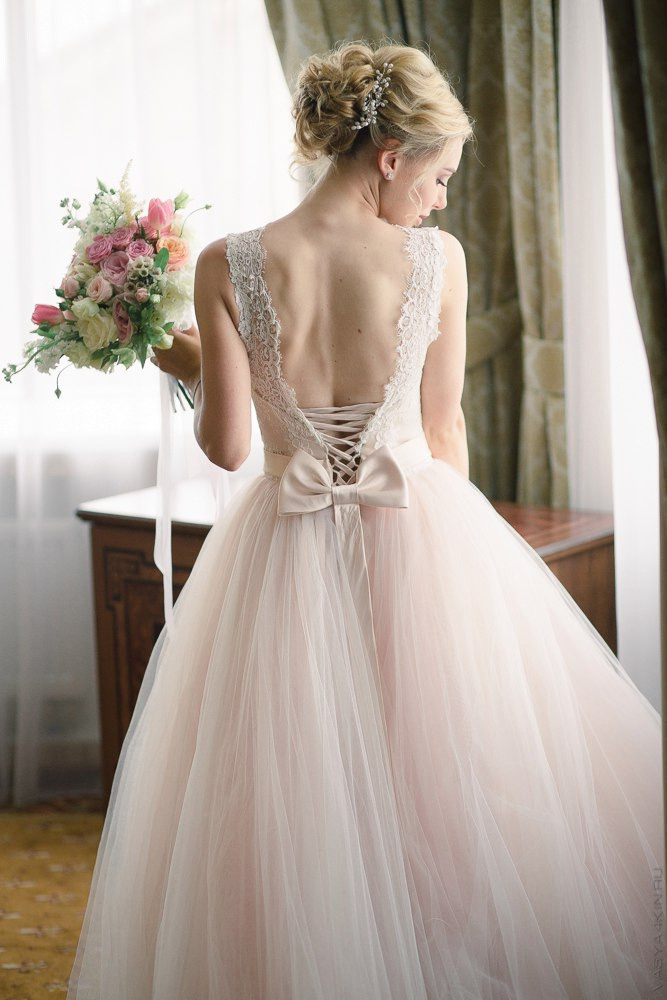 Невеста в длинном белом платье прогуливается по дорожке, обрамленной фонтанами, на своей роскошной свадьбе в Ярославле