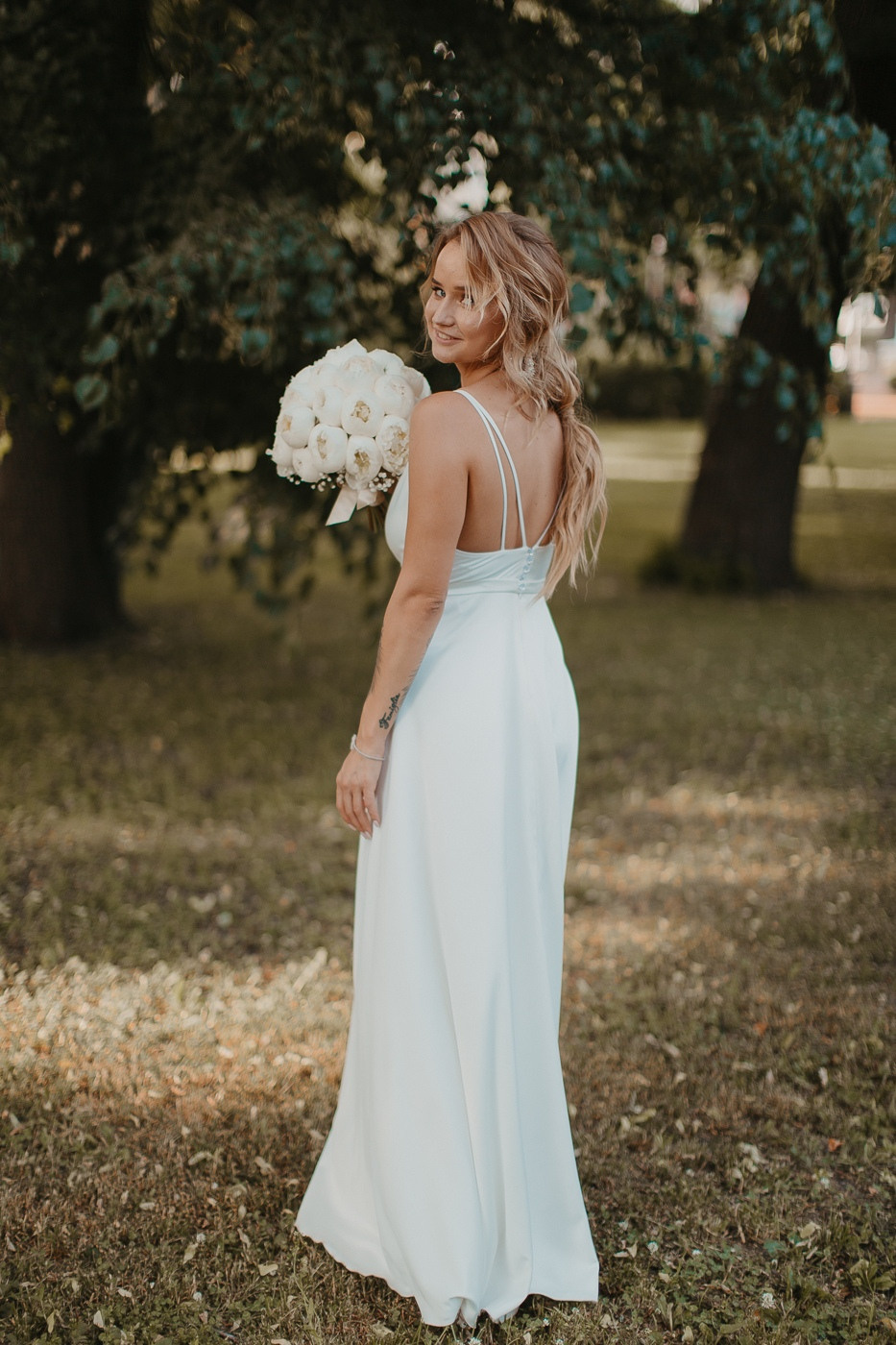 На снимке запечатлено крупным планом белоснежное свадебное платье невесты, развевающееся на ветру на фоне дороги