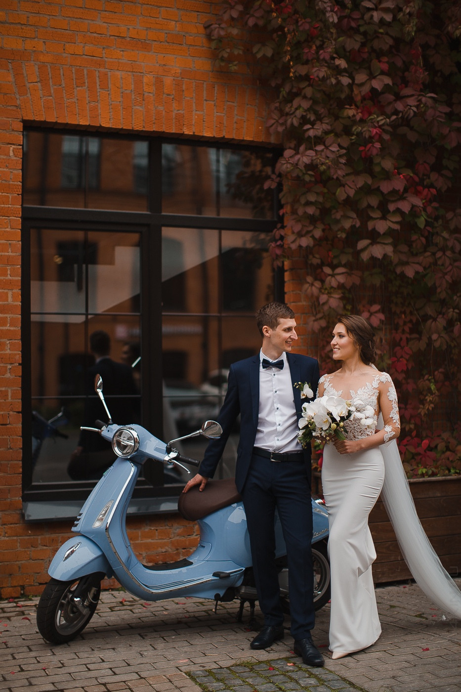 Молодая пара, сидящая на берегу озера, с пучками нежно розовых и белых цветов вокруг