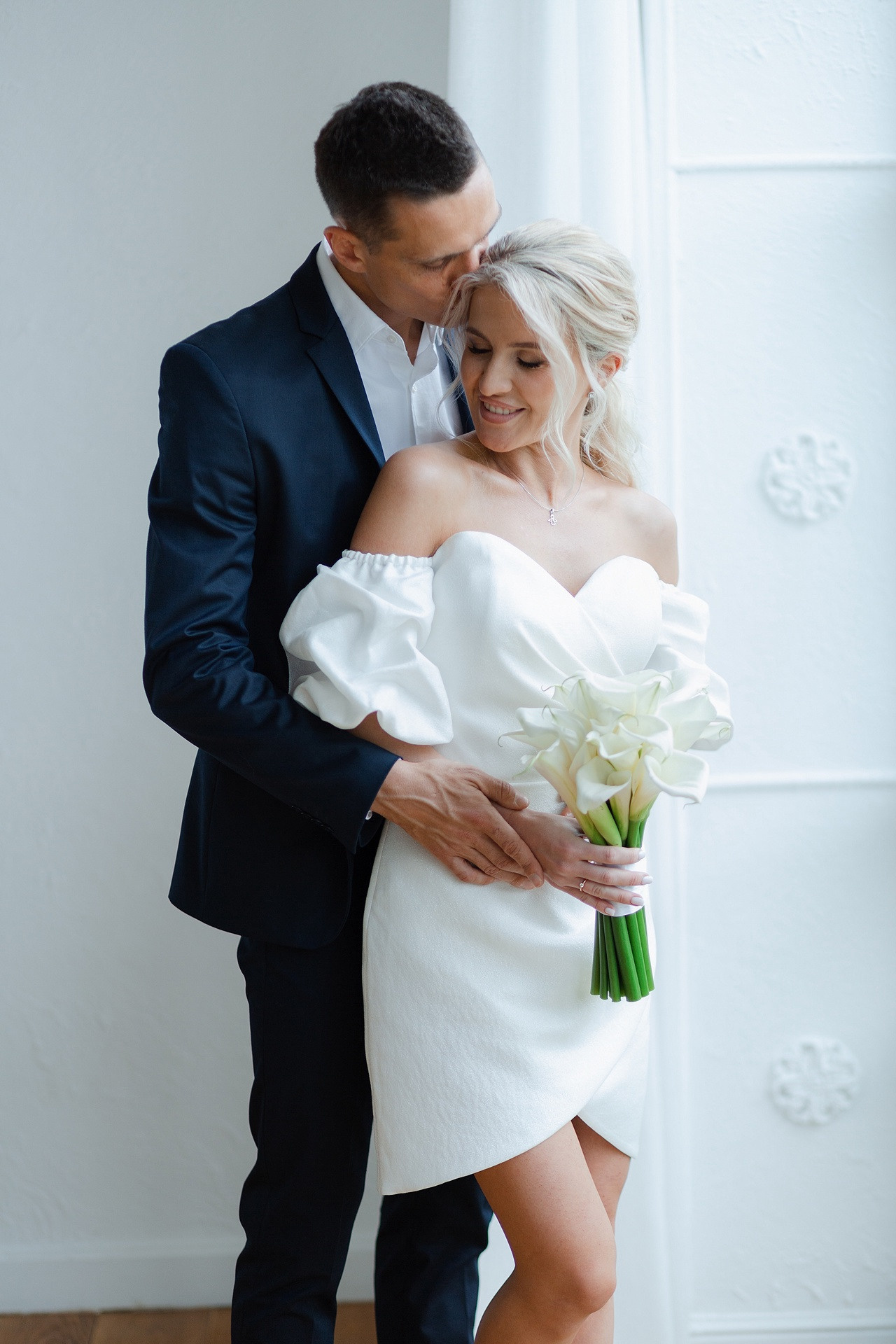 Молодожены идут по аллее с пышными деревьями и фонтанами, освещенными вечерним светом, на своей гламурной свадьбе в Ярославле