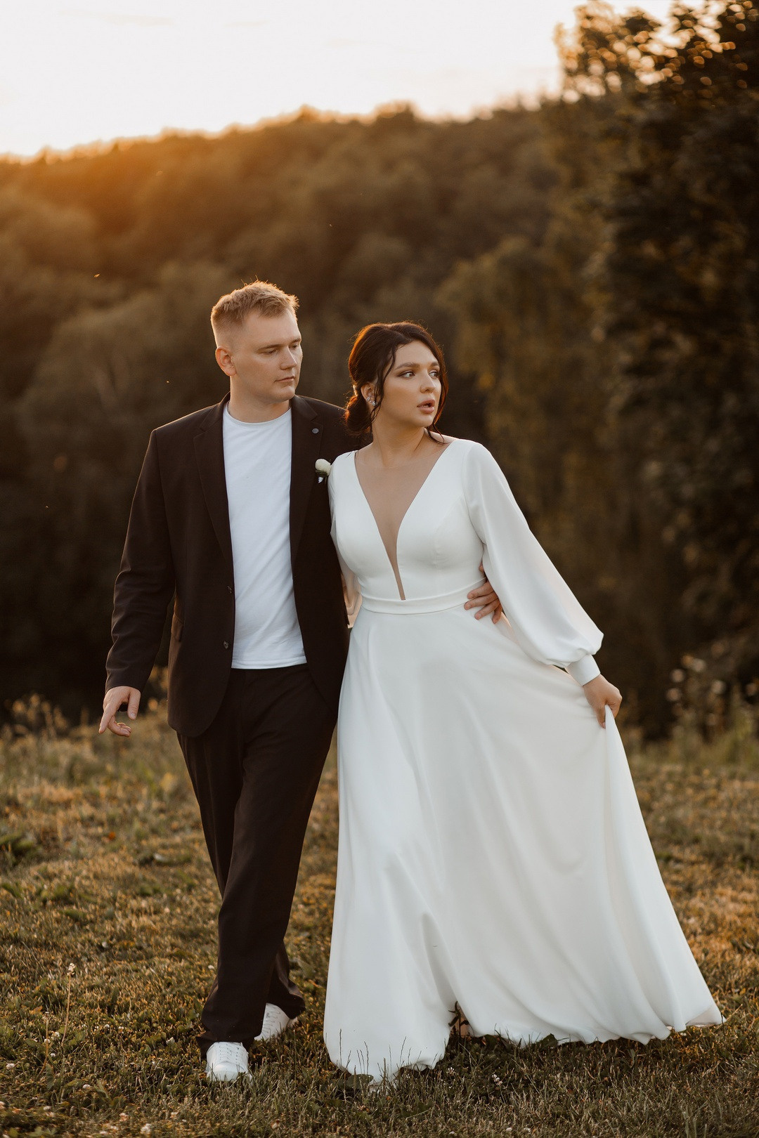 Невеста и жених сидят на поляне, окруженной цветущими деревьями, создавая атмосферу весенней свежести и начала новой жизни