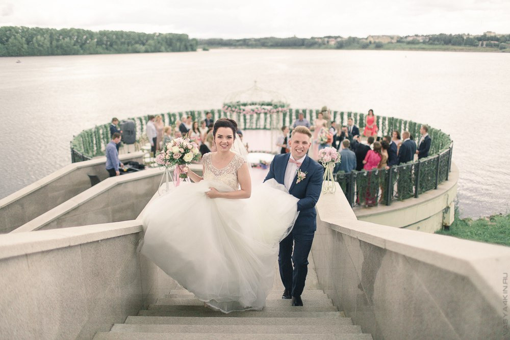 Невеста и жених позируют на фоне винного погреба с фруктовыми композициями, символизирующими плоды их любви