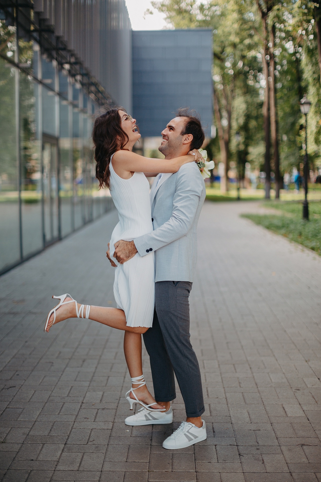 Невеста и жених, держась за руки, идущие по лесной тропинке, окруженные деревьями и цветами, создавая атмосферу уюта и приватности