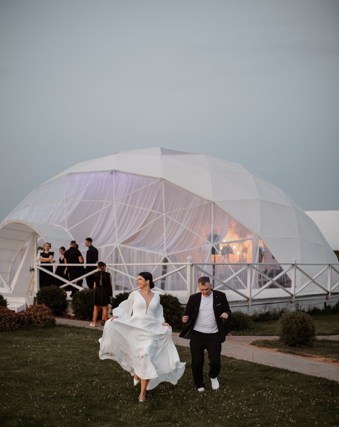 Фотография с гламурной свадьбы в Ярославле, где невеста и жених идут по дорожке, обрамленной гранитными колоннами, увенчанными цветочными композициями
