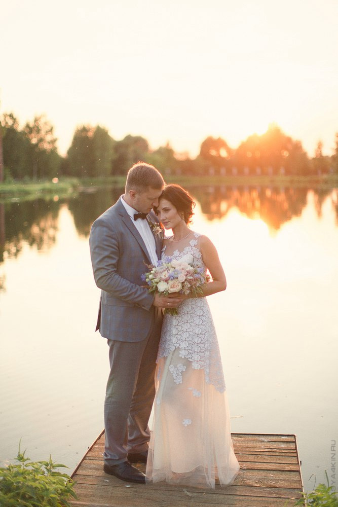 Романтическая сцена, когда невеста и жених, разделяющие подвеску в форме сердца, смотрят на заходящее солнце