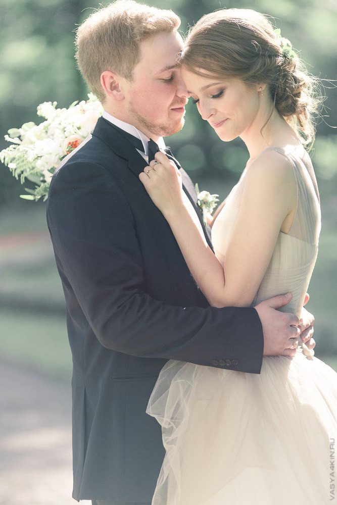 Невеста, улыбающаяся в фотообъектив, когда ее жених поцеловал ее на лугу, покрытом полевыми цветами