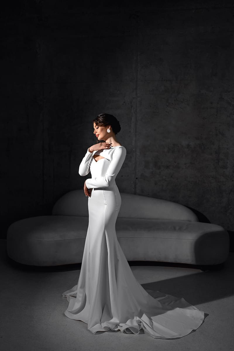 Женщина в белом платье стоит у дивана