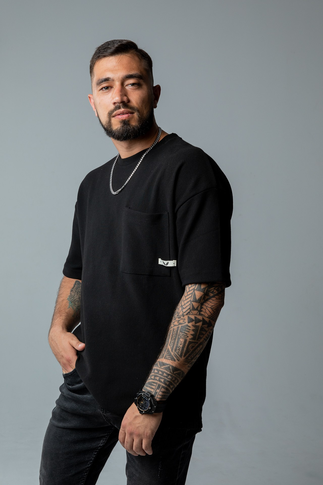 Мужчина брюнет с бородой в черной футболке и джинсах