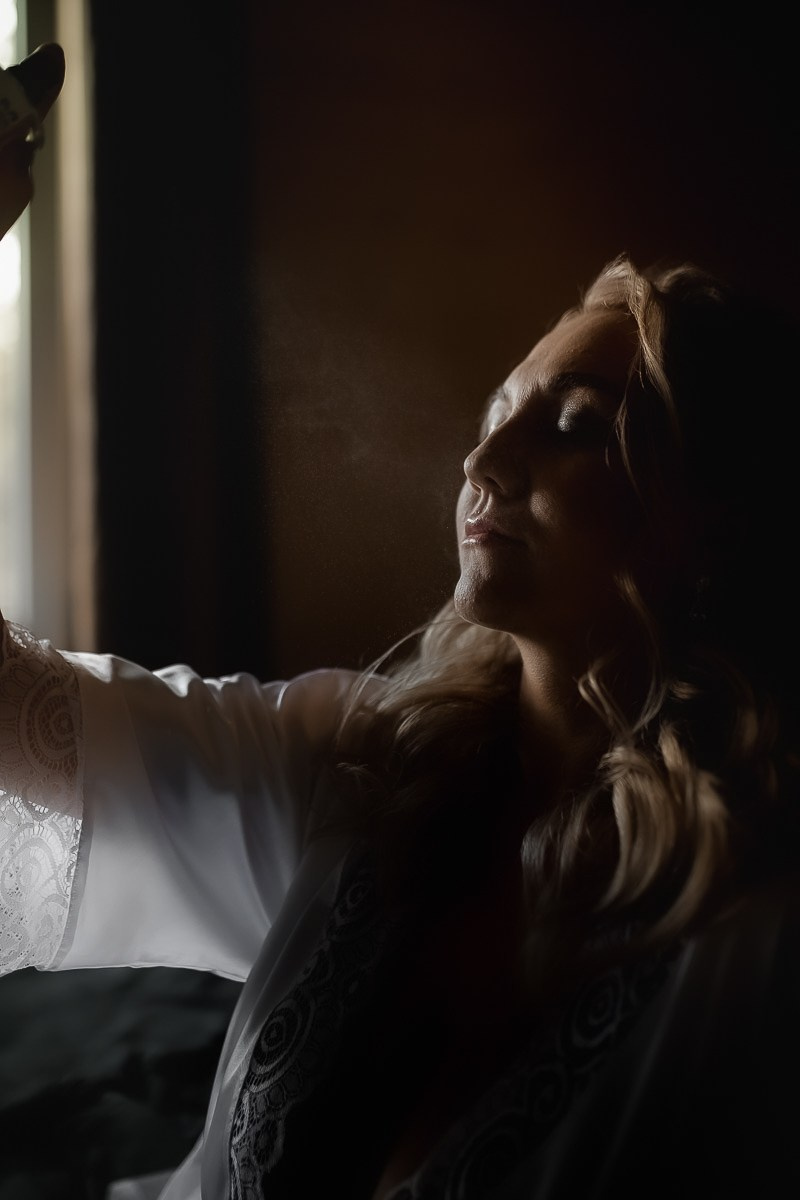 Невеста брызгает на себя духами в контровом свете в комнате в Санкт-Петербурге