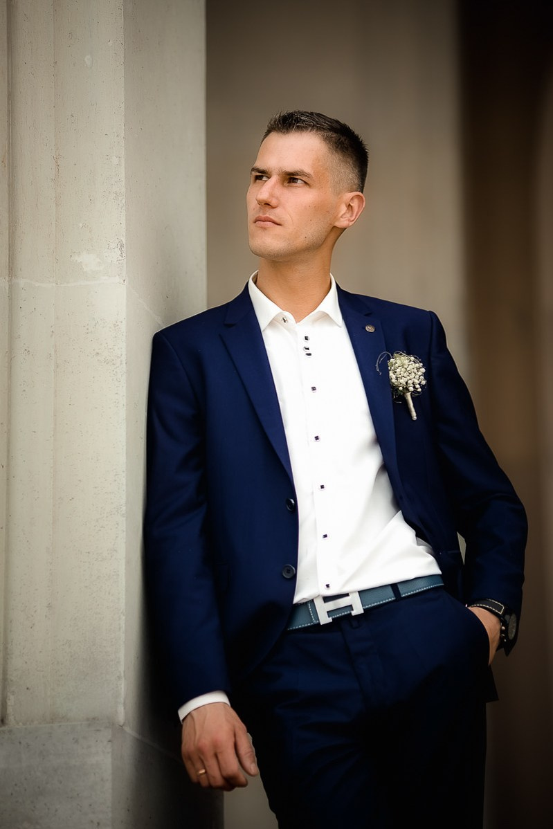 жених смотрит в даль, стоя на крыльце заксобрания в Санкт-Петербурге. Рука в кармане. Вертикальный поясной портрет.