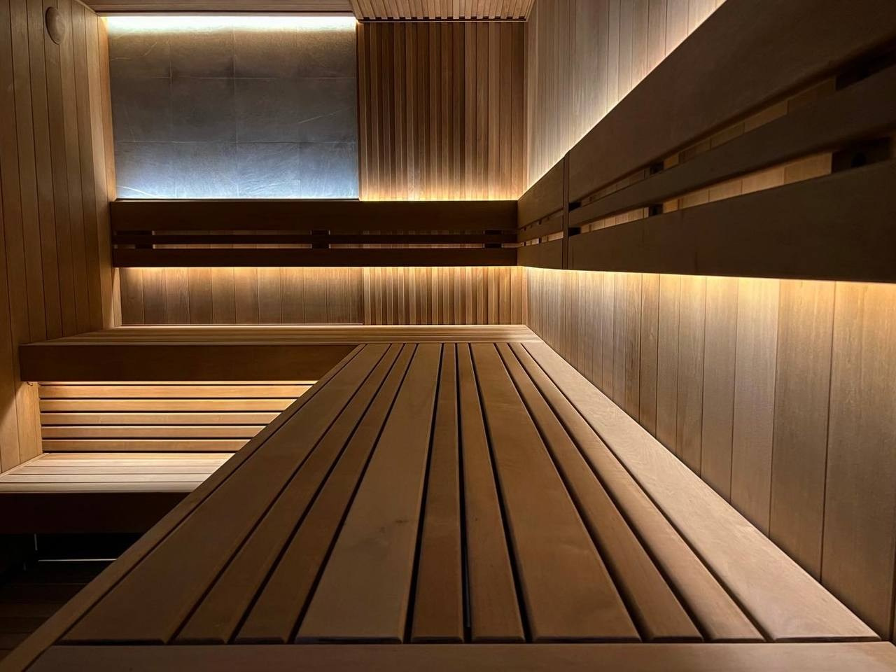 Сауна в Керро из разноширокой термоольхи. Ламповый свет термостойких лент и закарнизная подсветка плитки из талькохлорита 300×300мм. SaunaTopMasters