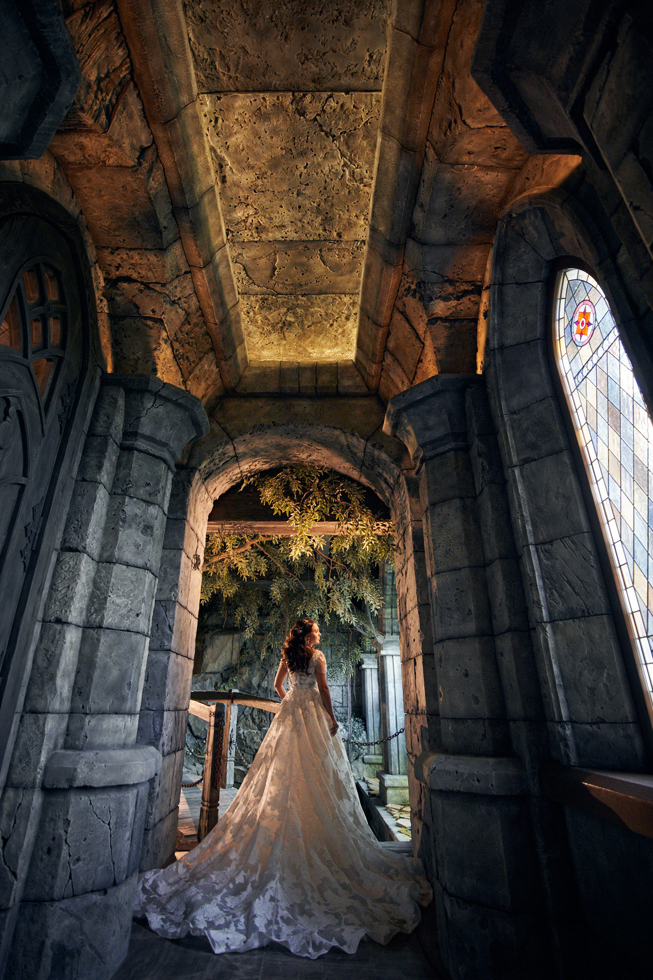 “Портретная съемка в замке Гарибальди – модель в роскошном наряде позирует у старинного окна с витражами.”