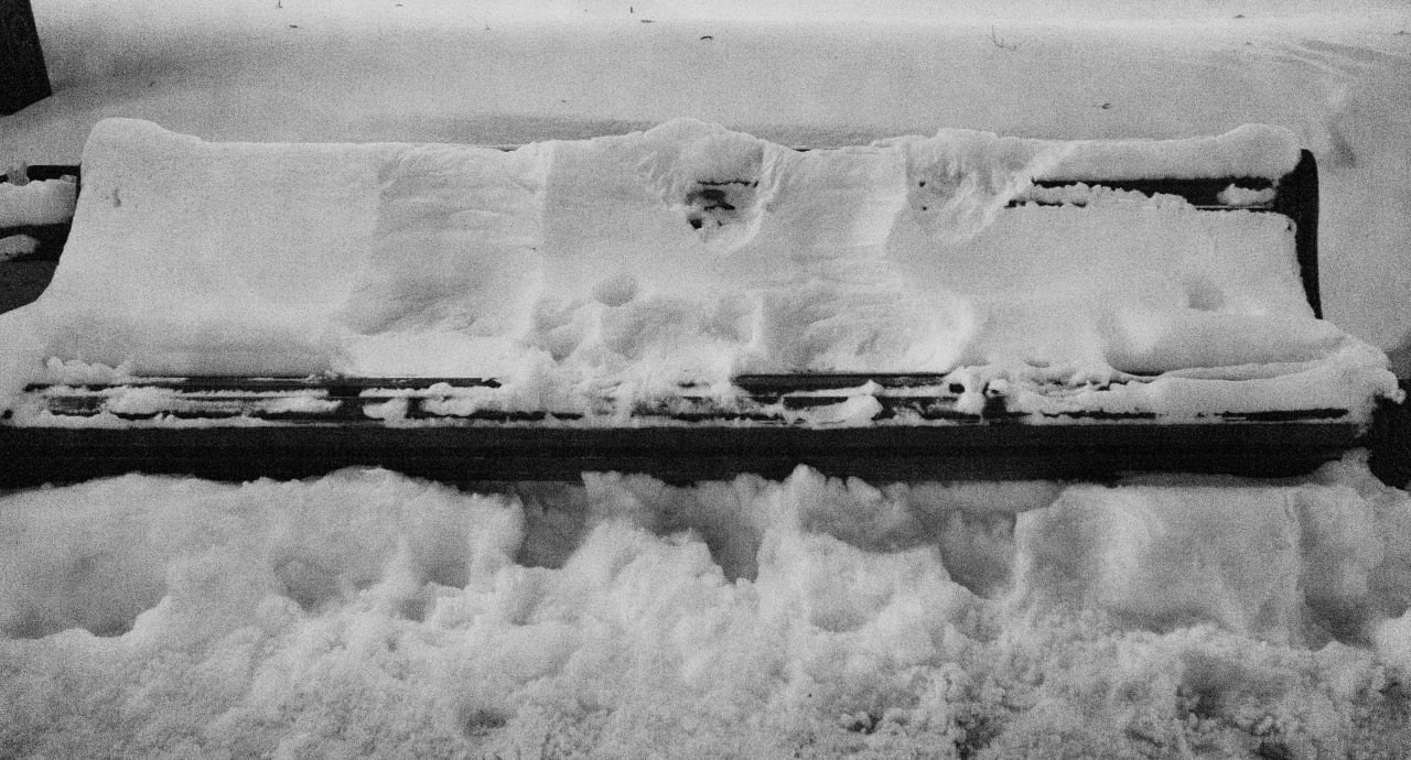 Черно-белая минималистичная уличная фотография: массивный снежный покров и ледяная корка скрывают горизонтальную конструкцию, оставляя лишь тёмную узкую полосу внизу, высокий контраст белой текстуры и чёрной линии, зимний городской пейзаж Москвы, Вадим Топорёнок, проект Манифест теней, городская тишина, архитектура снега, монохромная съёмка, визуальная пауза, урбанистический минимализм.