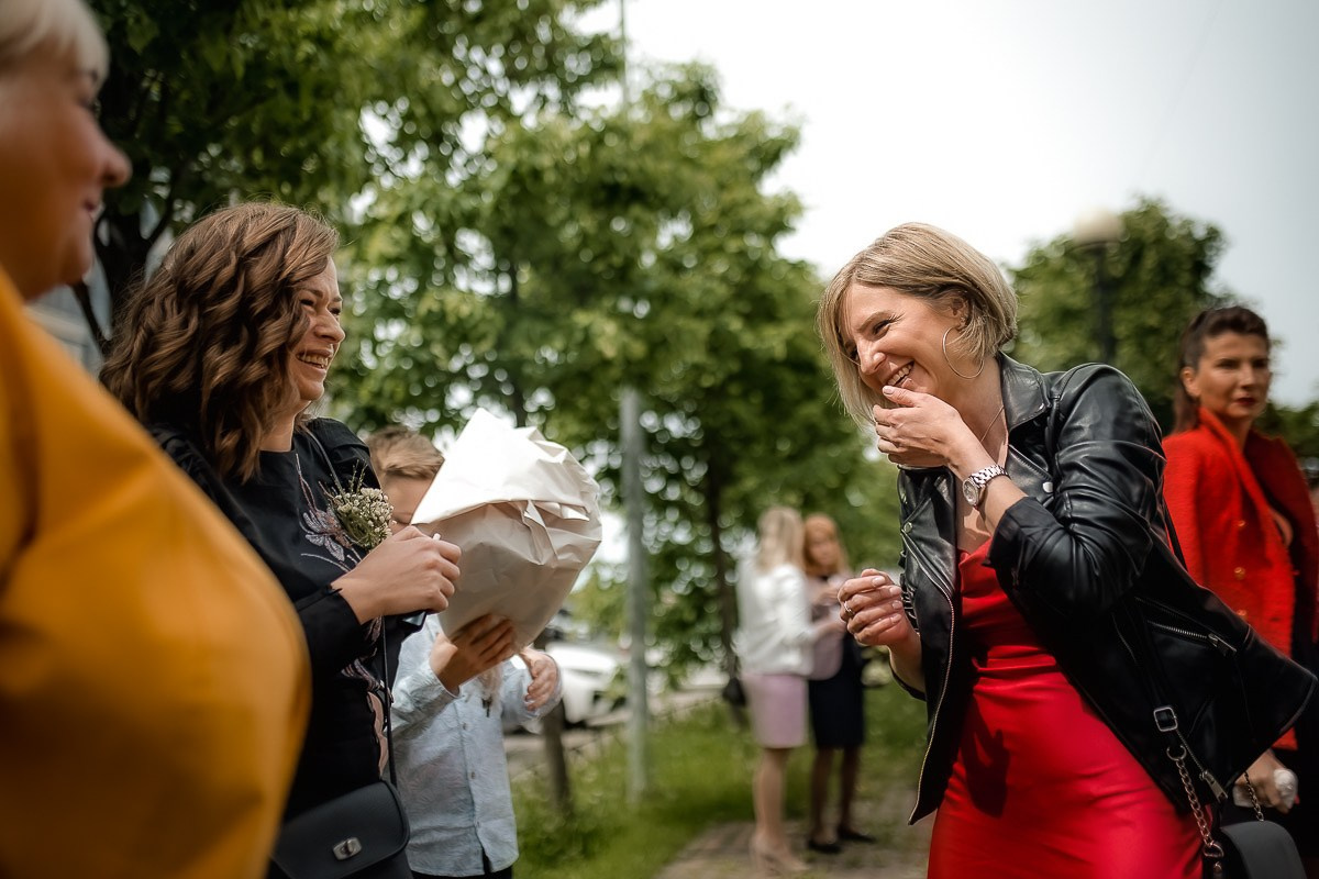 гости свадьбы смеются на фоне ЗАГСа на Васильевском острове в Санкт-Петербурге. Горизонтальный поясной кадр.