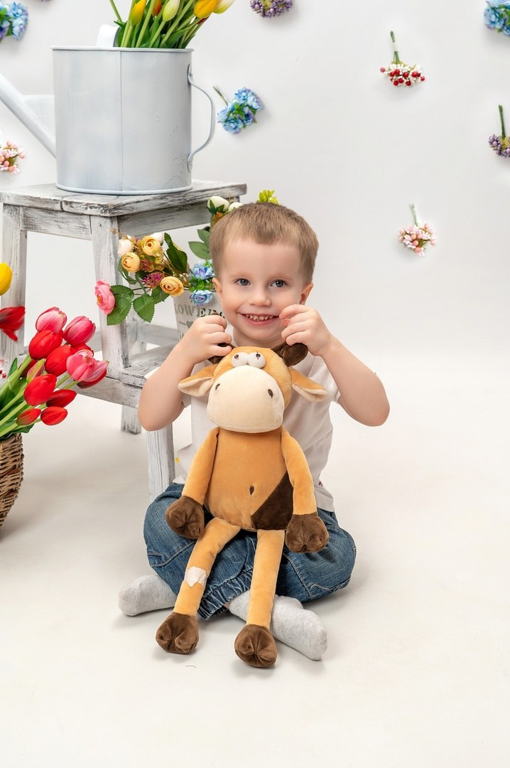 Мальчик с игрушкой мило улыбается на фотокамеру.