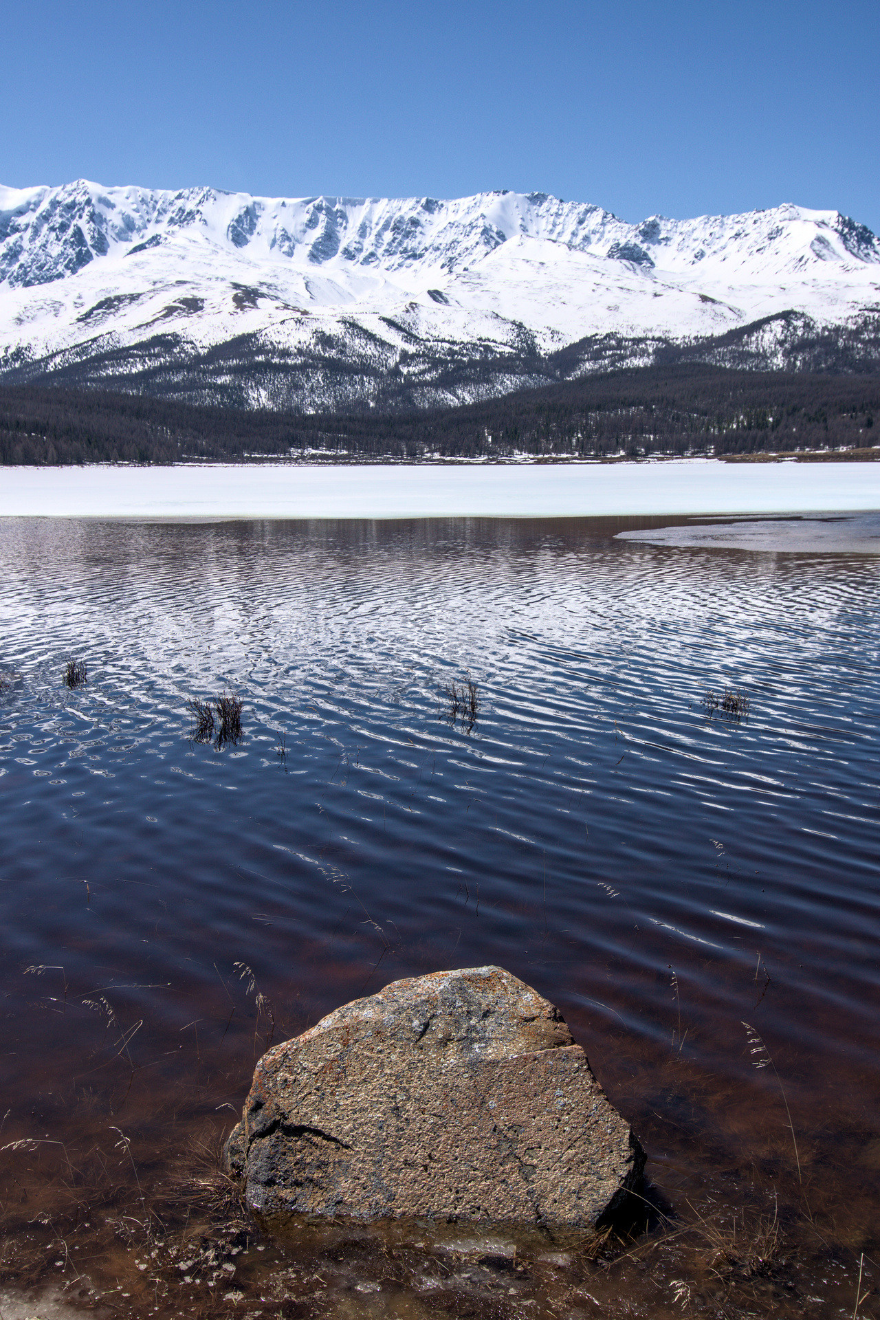 Камень в озере каракол с горами на заднем плане