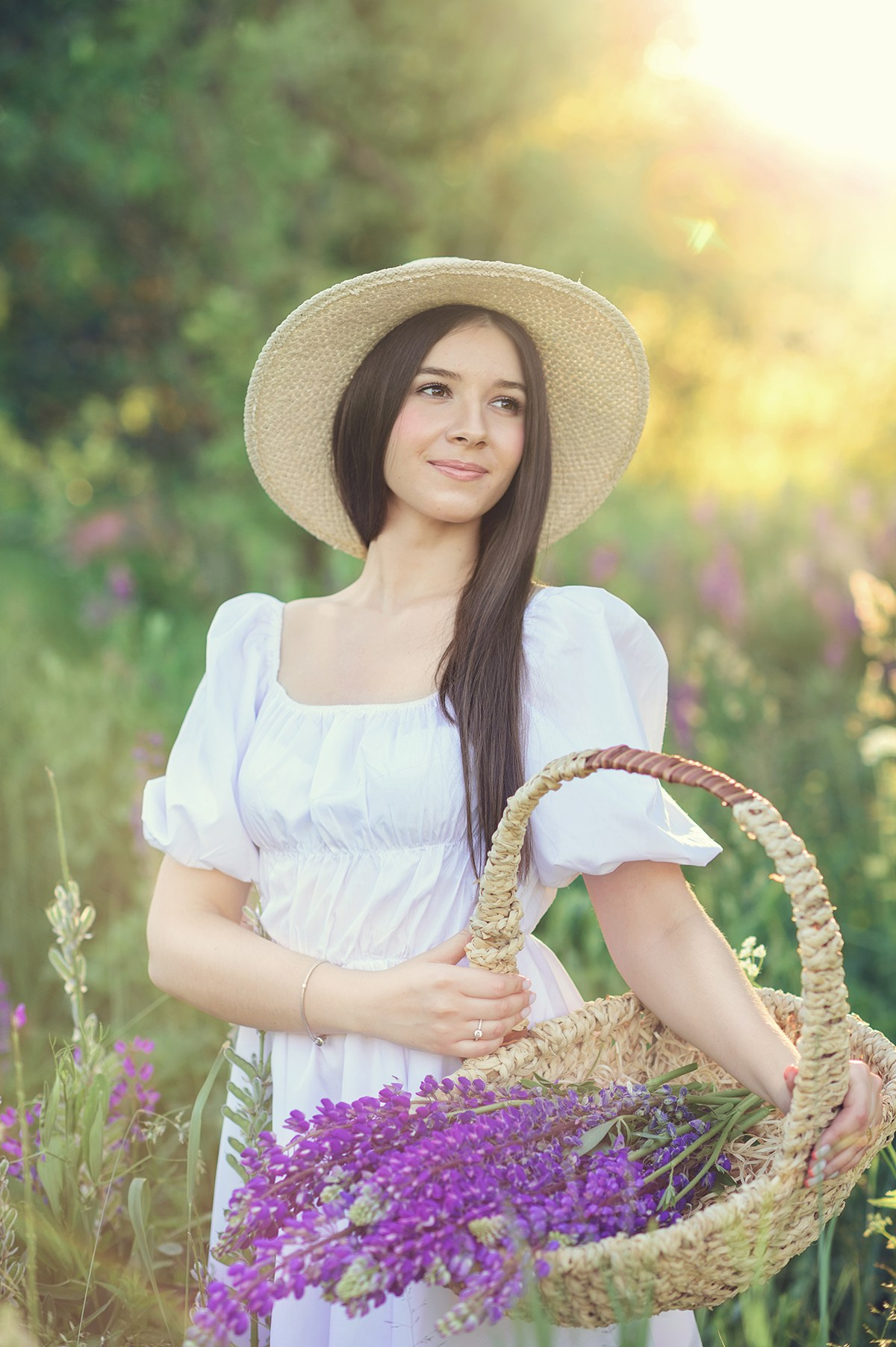 Молодая красивая девушка на закате в люпиновом поле держит в руках корзину с люпинами