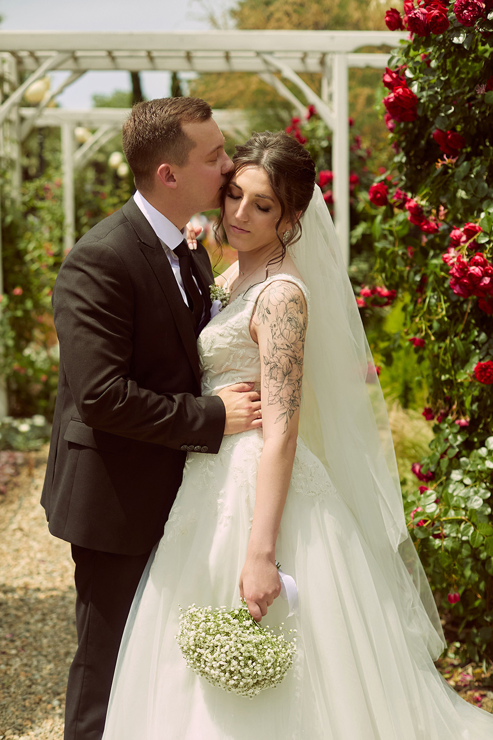 Невеста и жених обнимаются в парке возле розового куста. Фотограф. Тимашевск. Кубань. Краснодарский край.