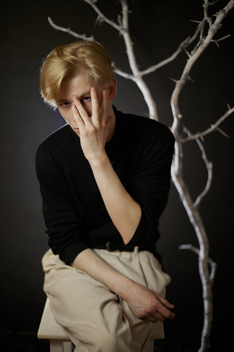 Парень сидит на белом стуле и закрывает лицо на фоне белого сухого дерева на черном фоне. Фотограф. Тимашевск. Кубань. Краснодарский край. Москва. Фотограф в Москве.