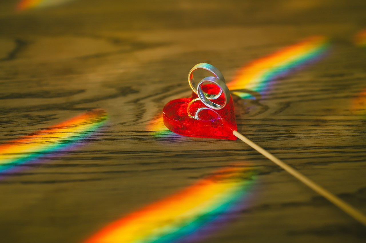 обручальные кольца на красном леденце в виде сердца в радужных бликах 