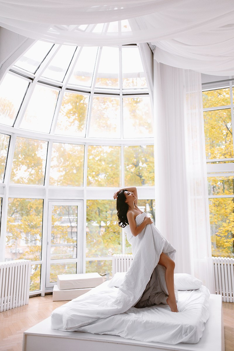 Леди в белом одеяле стоит на кровати под куполом