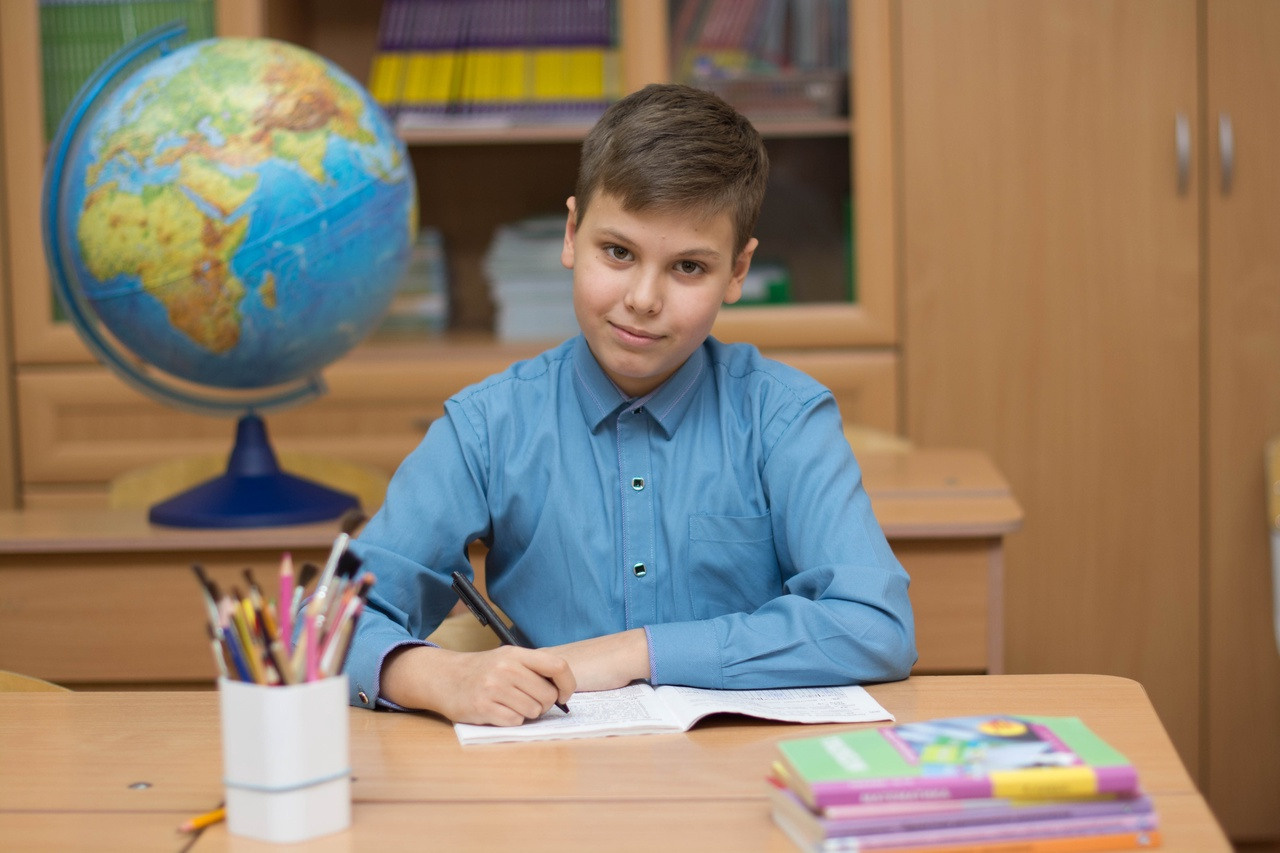 Парень в голубой рубашке сидит красиво за партой.