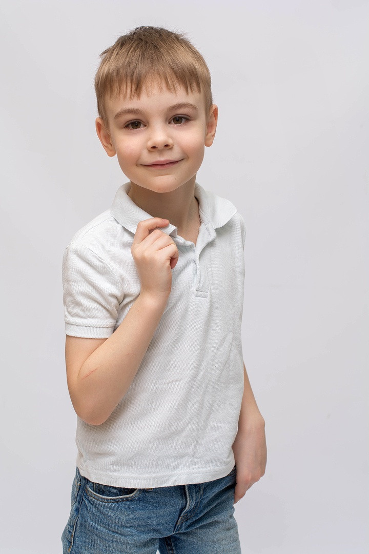 Мальчик в белом поло стоит один и улыбается.