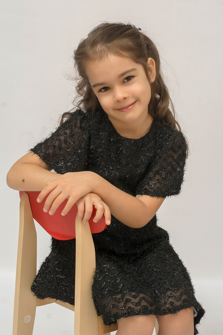 Черное платьице милое личико девочка сидит в группе.