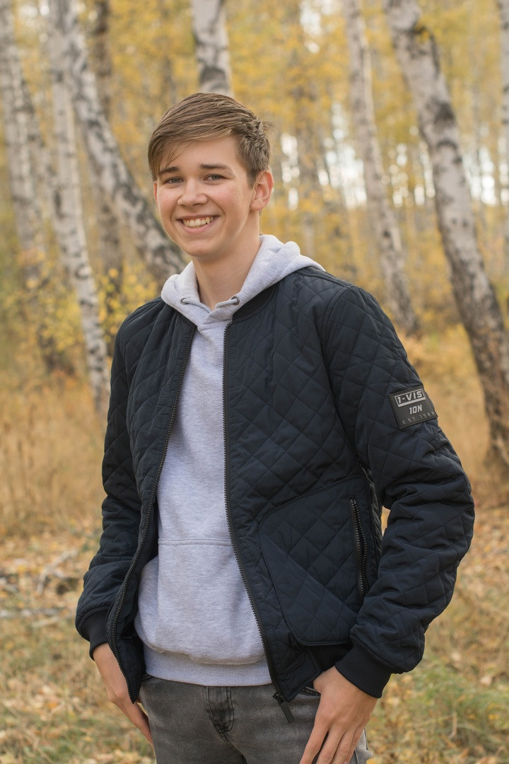 На природе в курточке стоит веселый паренёк.