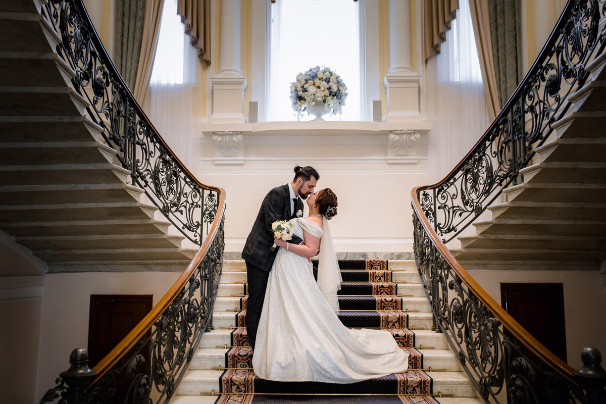 Жених и невеста целуются на лестнице в ЗАГСе на фурштатской СПб. Горизонтальный кадр