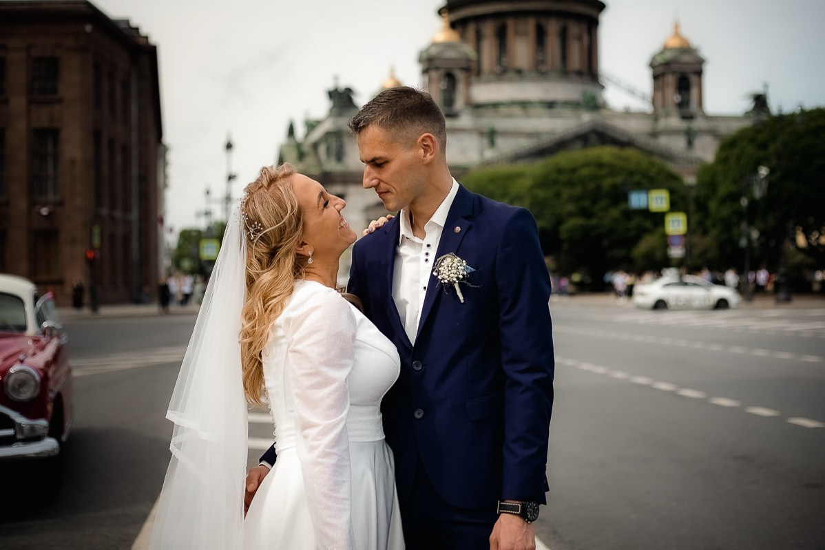 Жених и невеста смотрят друг на друга на фоне Исаакиевского собора в Санкт-Петербурге. Горизонтальный  поясной кадр.