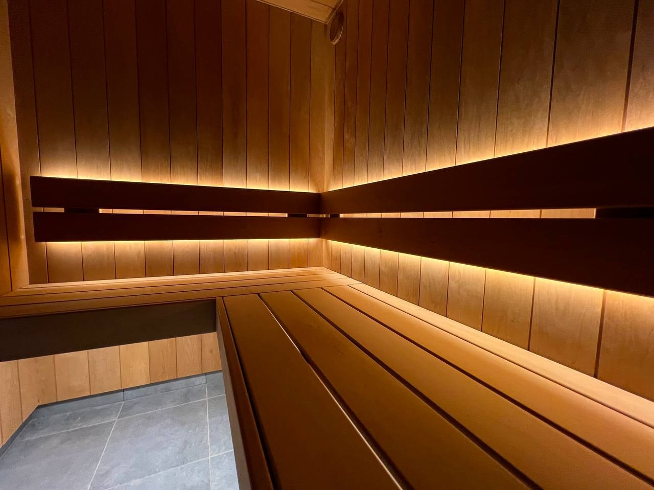 Уютная парная в Колтушах: внутренняя топка, печь в редкой облицовке, термоольха и тёплая линейная подсветка. SaunaTopMasters