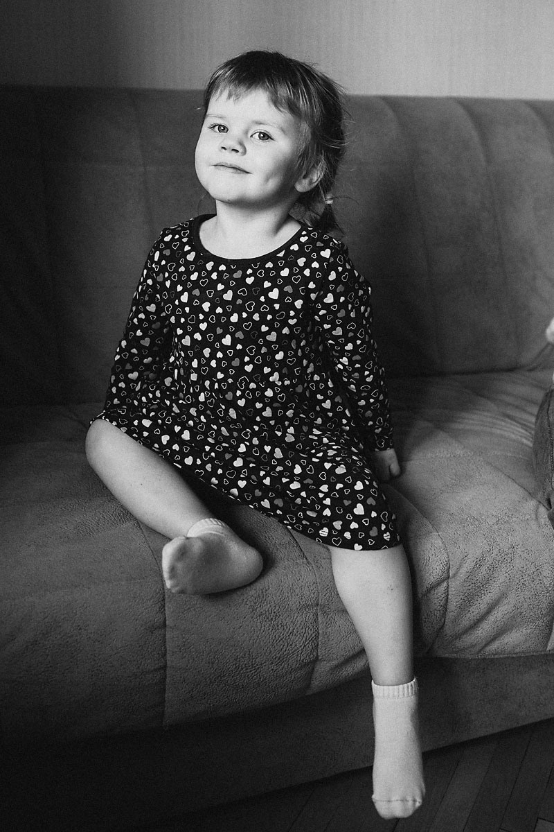 маленькая красивая девочка в летнем платье сидит на диване и улыбается