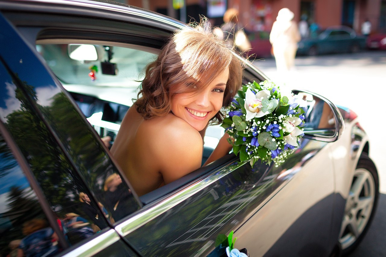 невеста с обнаженной спиной игриво выглядывает из окна черного свадебного авто