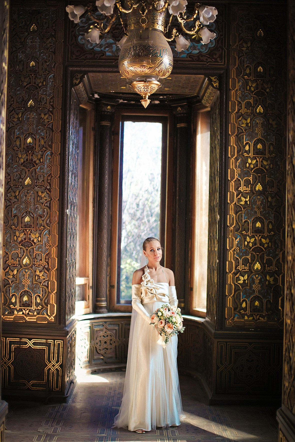 портрет невесты в дизайнерском платье на фоне хрустальной люстры в золотом зале дворца