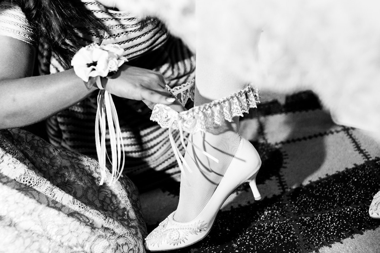 подружка невесты одевает подвязку на ногу невесты