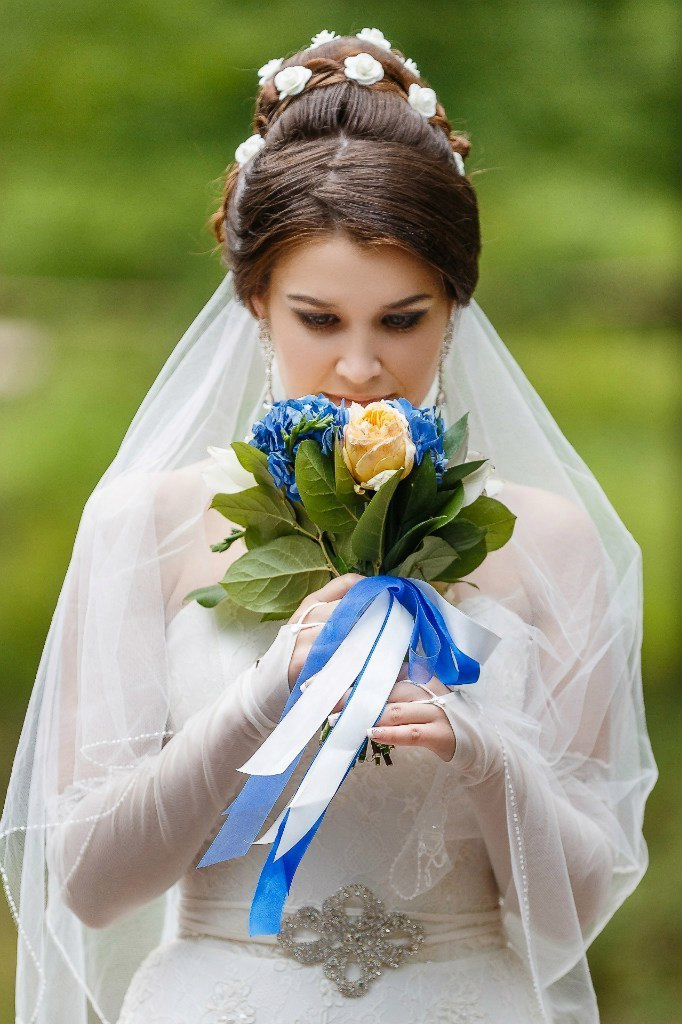 Невеста нюхает вкусный запах живого букета с бело синими ленточками