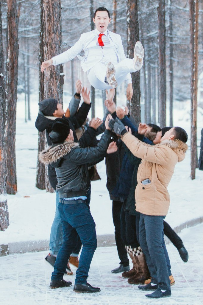 Друзья жениха подбрасывают жениха на фоне зимнего леса
