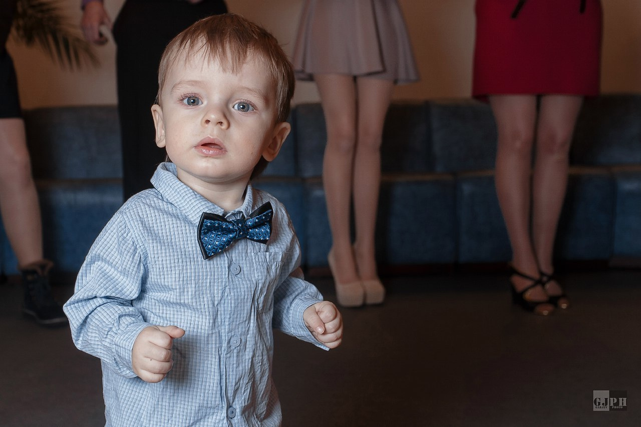 маленький мальчик позирует в загсе на фоне женских ног свадебных гостей