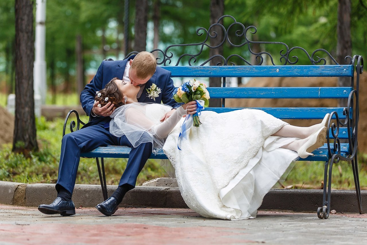 жених и невеста отдыхают лежа на лавочке городского парка