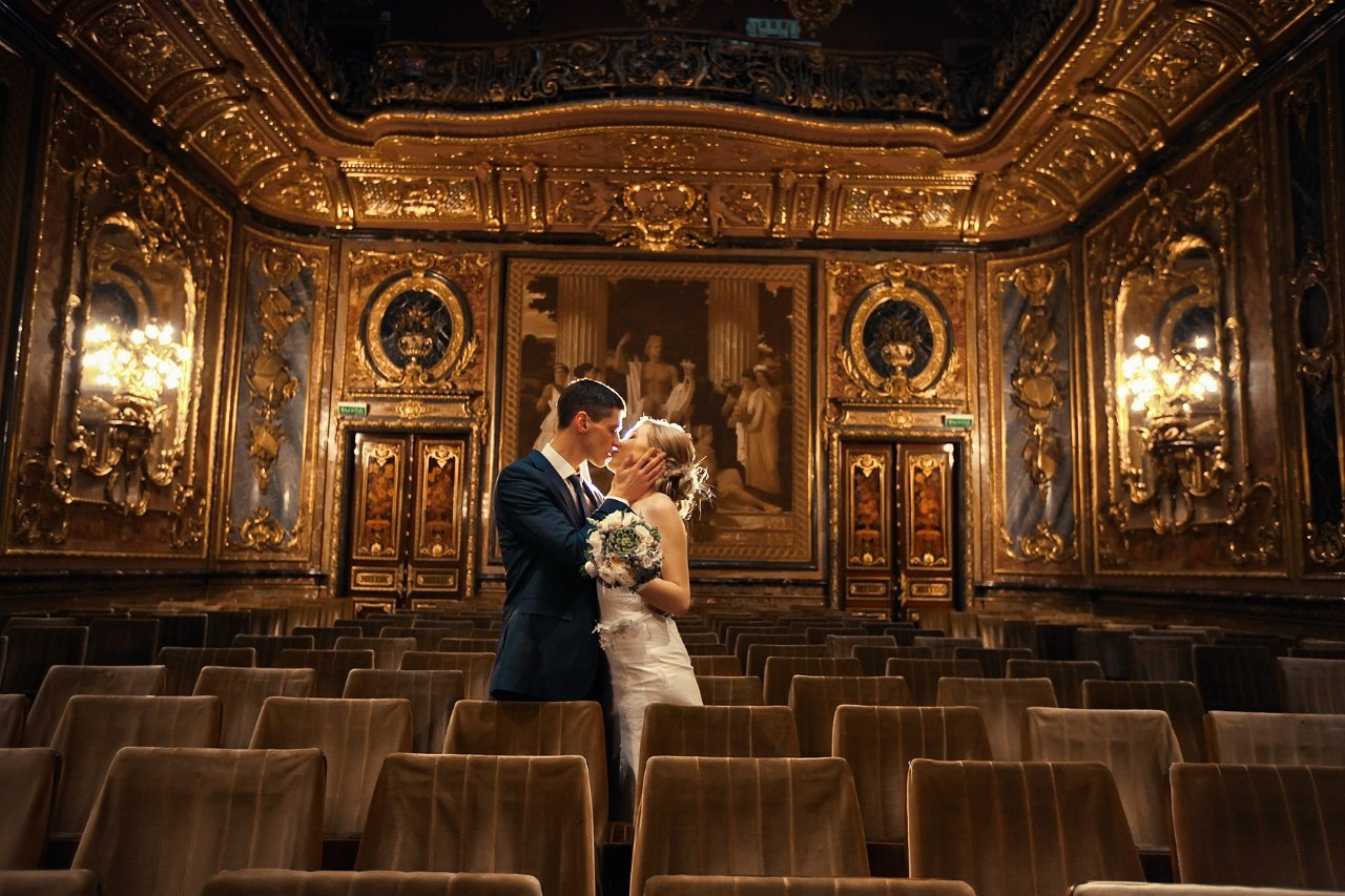молодожены целуются в тронном зале дворца с позолоченными стенами и потолком 