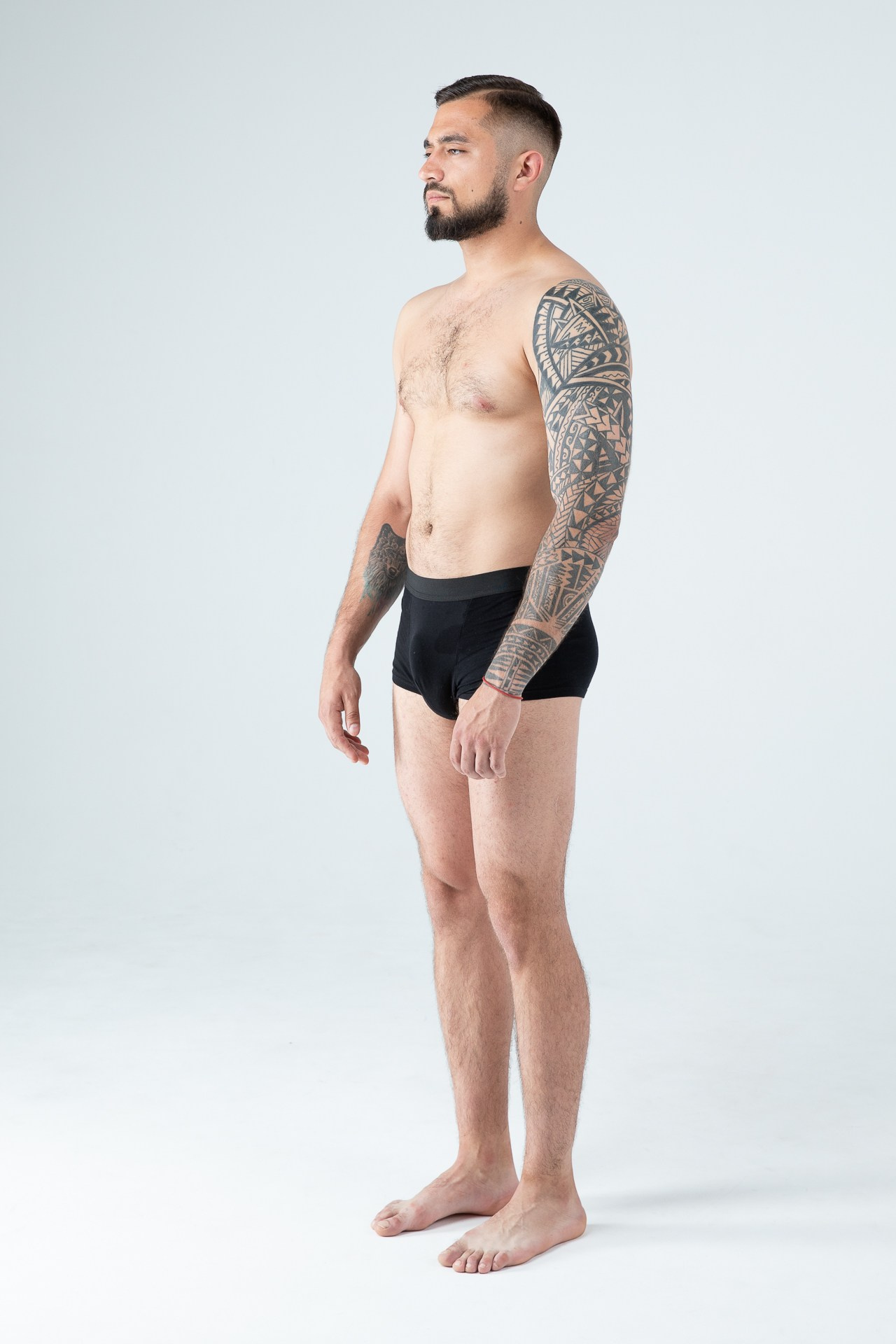 Мужчина модель с бородой с татуировками в черных трусах