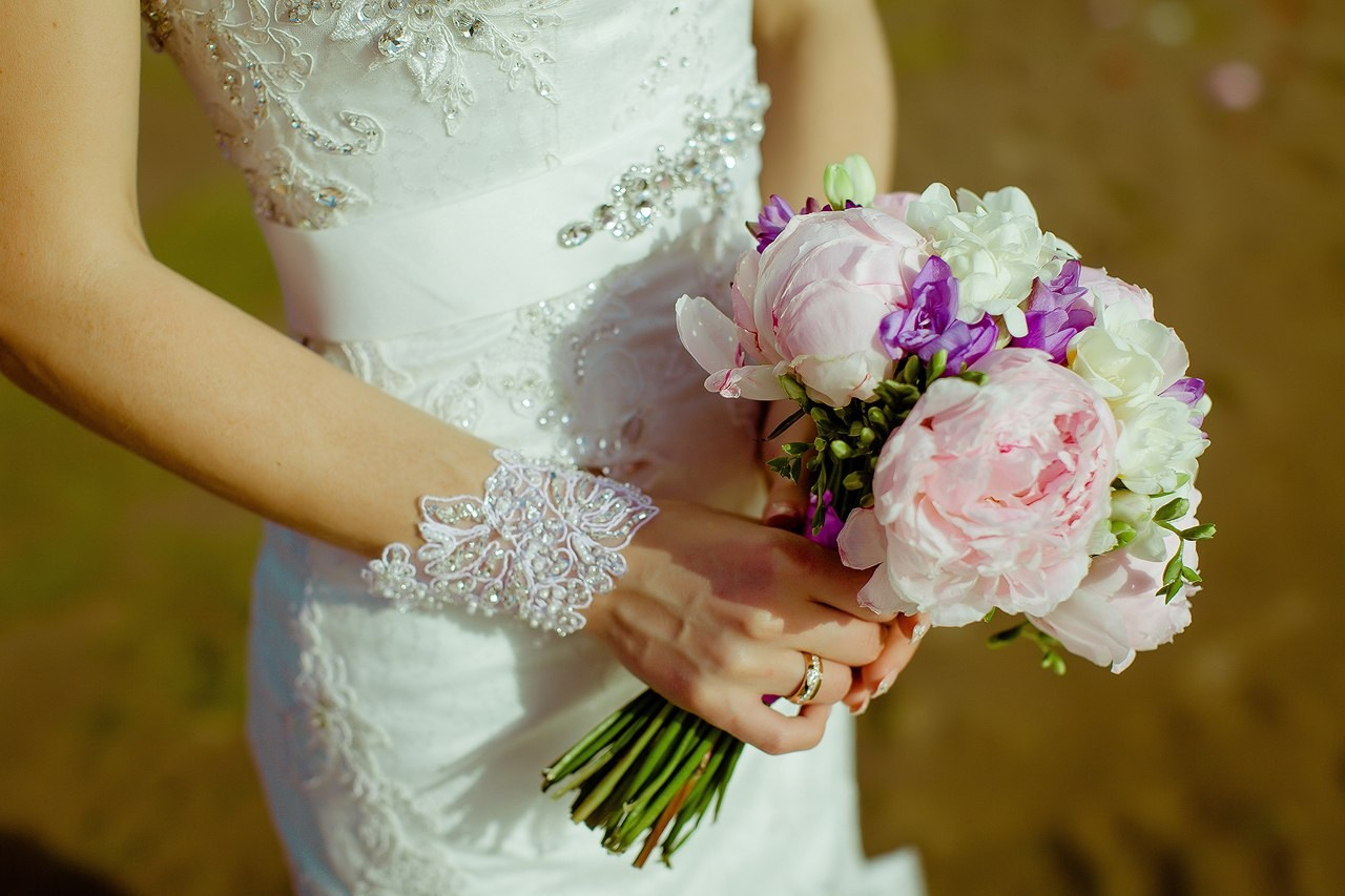 крупный план букета из пионов и обручального кольца на руке невесты в белом платье