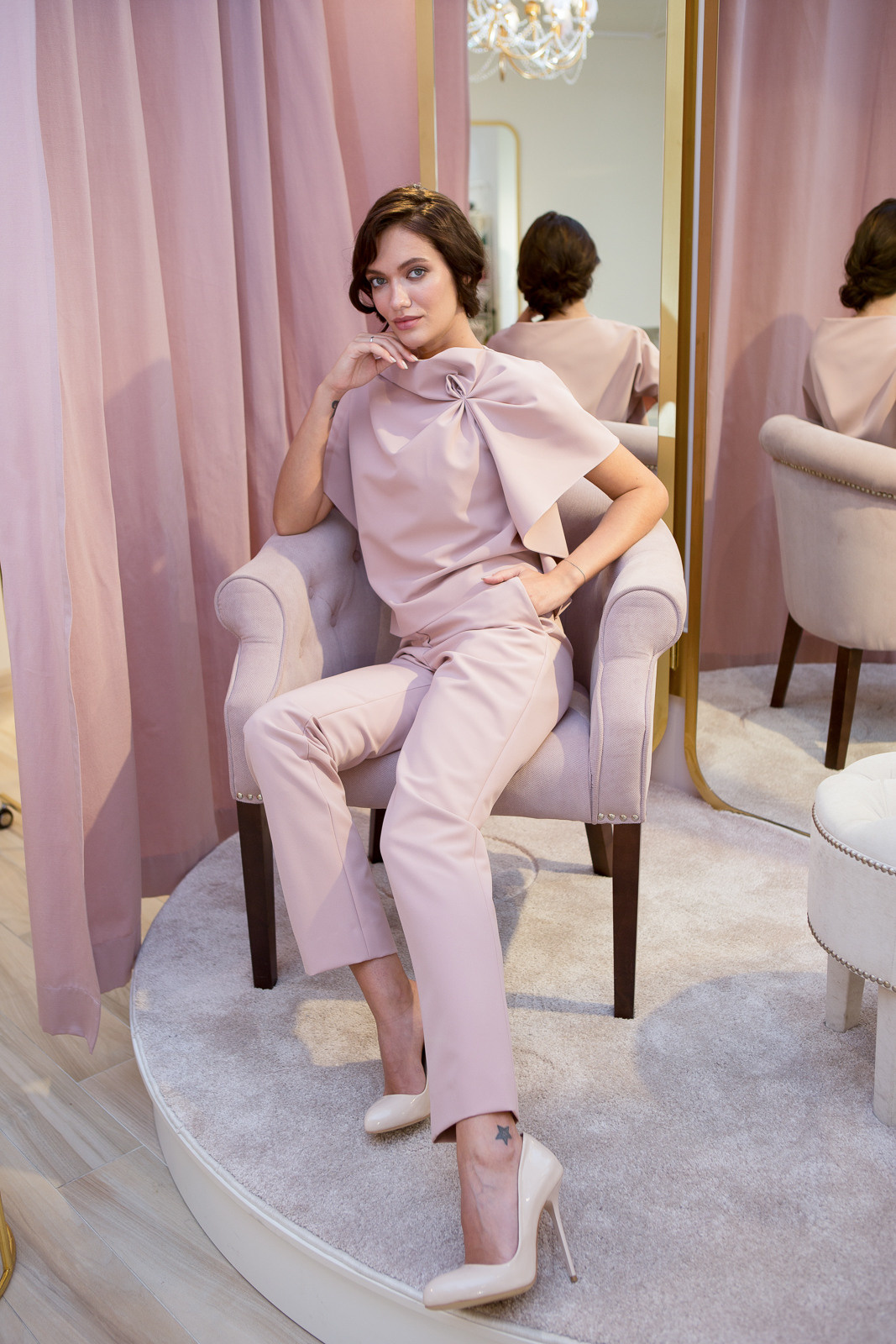 модель сидит на стуле в полный рост в розовом костюме 